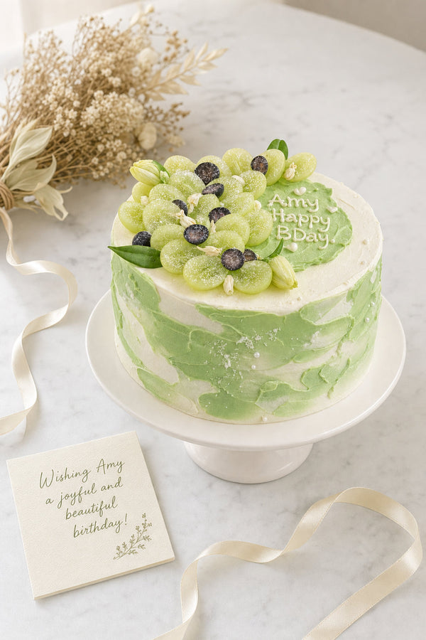 Round green ombré cake with textured buttercream topped with green grapes and dark berry slices on a white ceramic stand