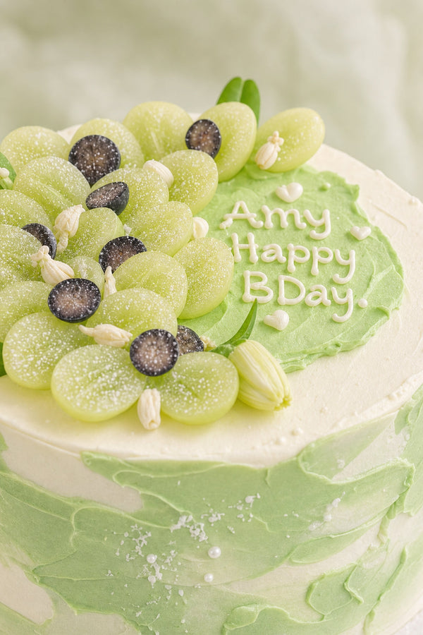 Side view of green ombré birthday cake decorated with fresh grapes and berries on white base