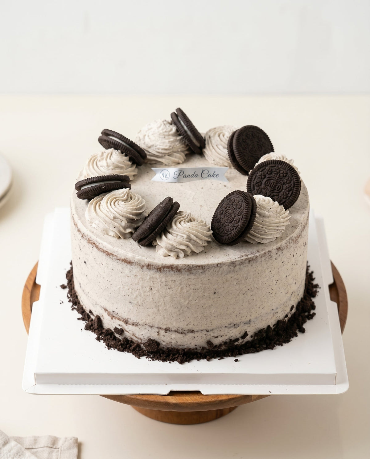 Round cookies and cream cake with smooth light speckled frosting, piped cream swirls and Oreo cookie decorations on top, photographed in a bakery setting.