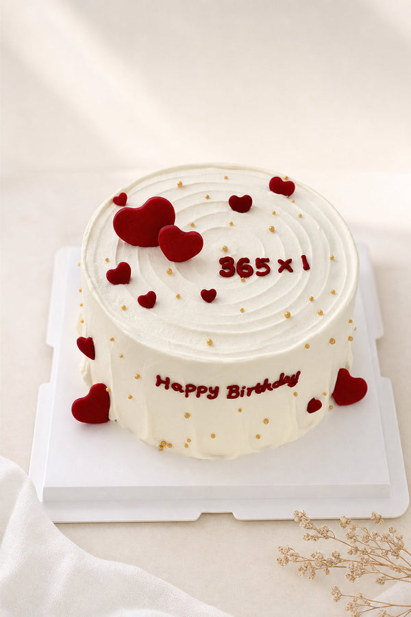 Studio shot of white frosted cake decorated with red hearts and gold pearl sprinkles, smooth spiral pattern on top