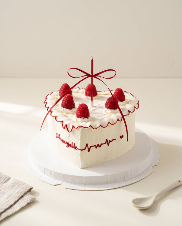 Round white buttercream cake with smooth textured icing and red scalloped piping along the top edge, set against a white background.