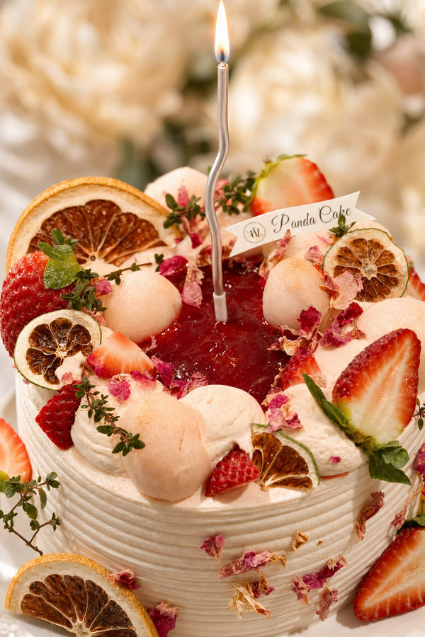 Round birthday cake decorated with sliced strawberries, dried citrus, and delicate rose petals on white frosting
