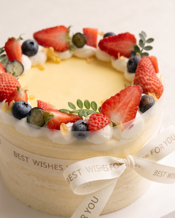 Side angle of tall round cake with smooth pale yellow cream and fresh berry topping