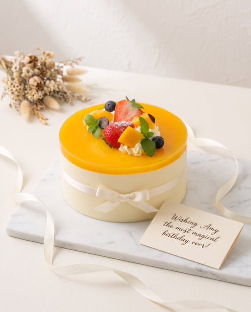 Round mango mousse cake decorated with vibrant fruit and glossy finish on white surface