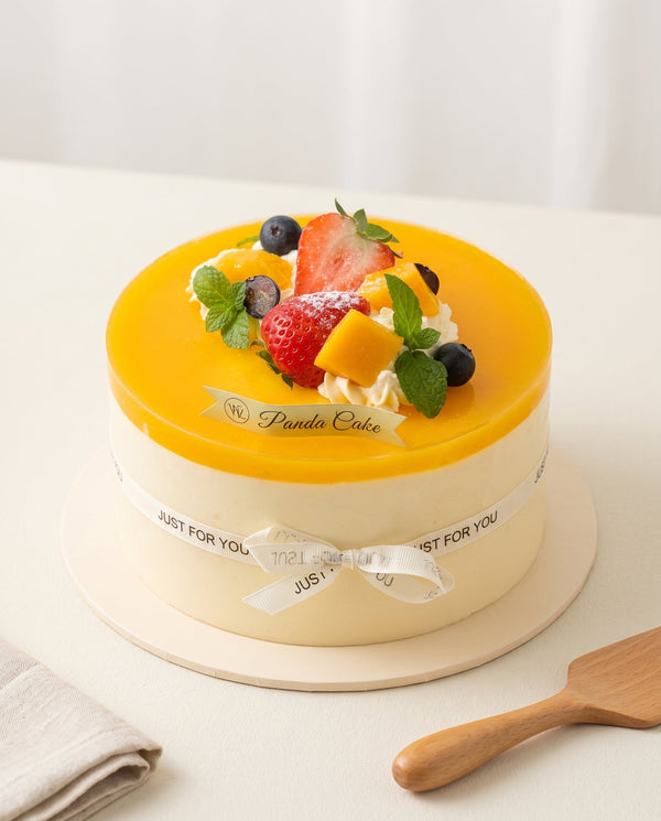 Premium studio photo of round mango mousse birthday cake with bright orange glossy glaze and fresh fruit topping
