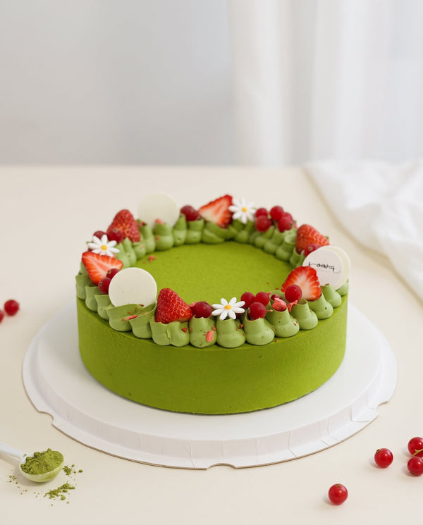 Studio shot of a round green matcha mousse cake with smooth matte surface and raised piped cream border topped with strawberries and berries