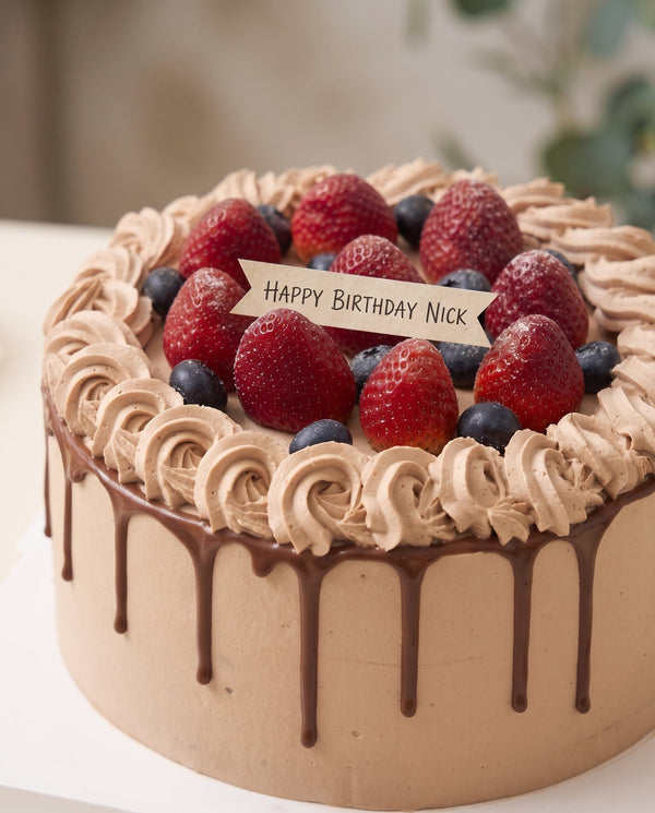 Round chocolate drip cake featuring taupe-brown buttercream rosettes topped with fresh strawberries and blueberries