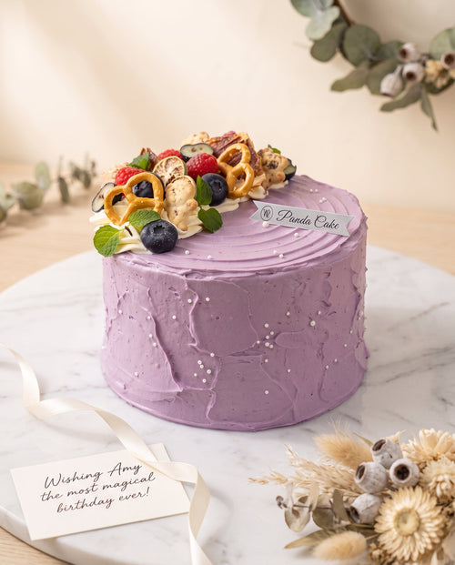 Side view of tall lavender buttercream cake with smooth textured frosting and scattered small pearl dragees