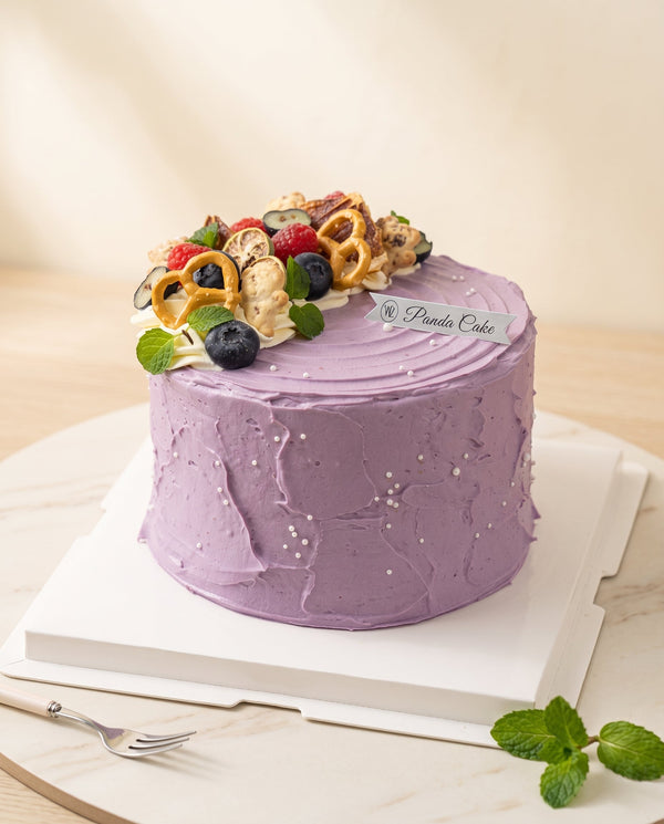 Studio product-hero image of a tall round lavender buttercream birthday cake with smooth concentric swirls and small pearl dragees on the sides