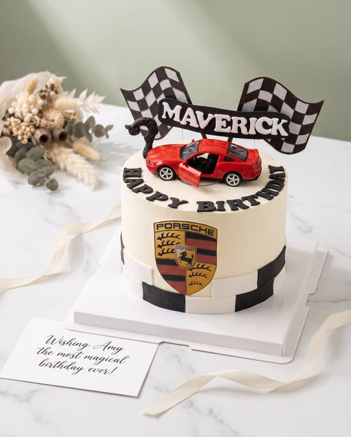 Motorsport themed birthday cake with smooth white icing and black pattern details topped with red sports car