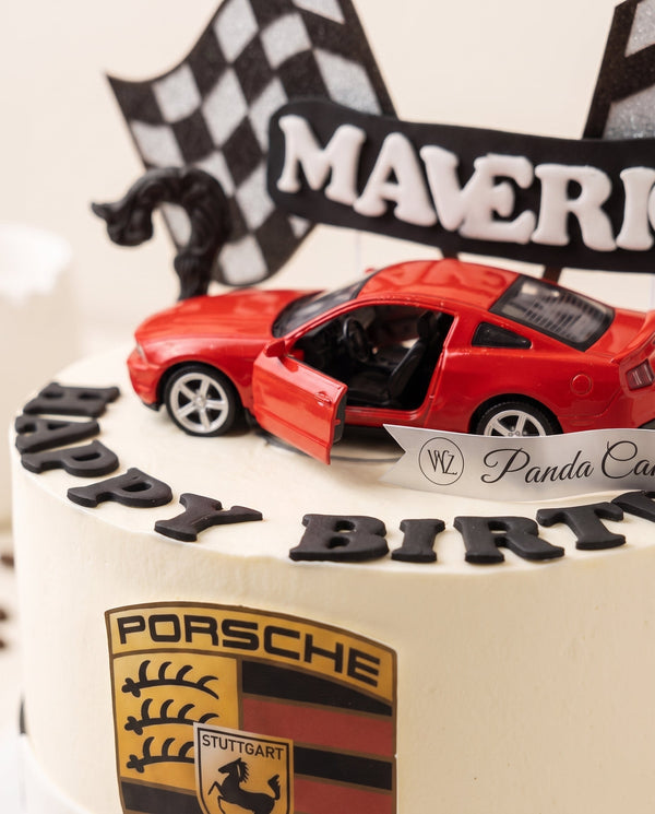 White cake decorated with black racing stripes, red car figure and Porsche logo