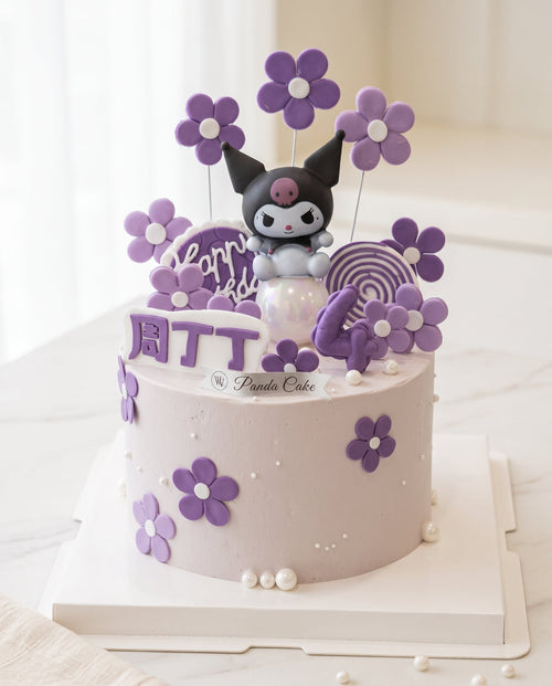 Studio photograph of a two-tier pale pink fondant cake decorated with purple flowers and pearl dragees featuring a Kuromi figure topper