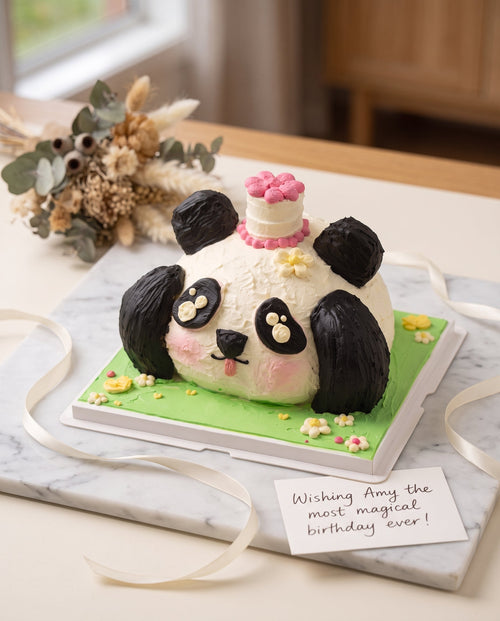 Close-up of panda face-shaped cake showing white buttercream frosting with black ears and eye patches