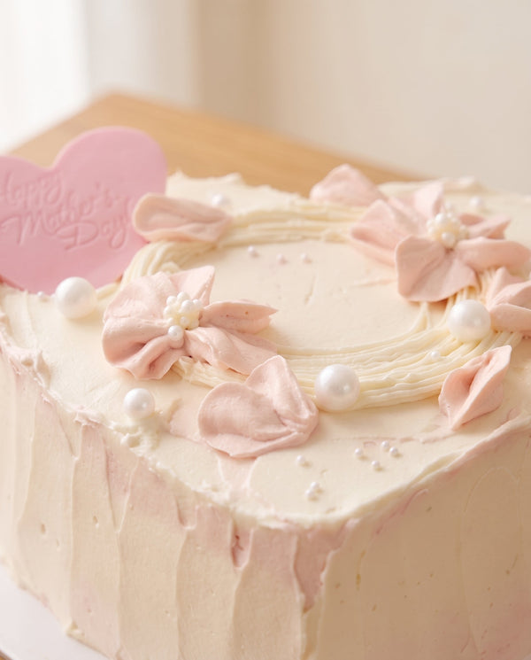Heart-shaped cake with white buttercream frosting, pale pink buttercream flowers, and pearl dragees
