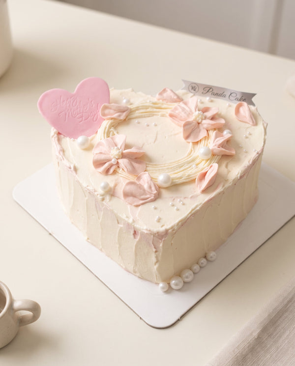 Studio photograph of heart-shaped white frosted cake decorated with pink buttercream flowers and pearl accents
