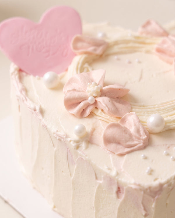 Close-up of heart-shaped cake featuring soft pink buttercream flowers and white frosting with pearl decorations
