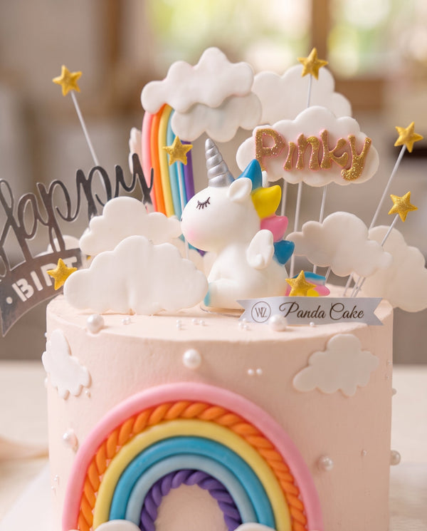 Round pastel pink unicorn cake showing rainbow front arch and white cloud decorations